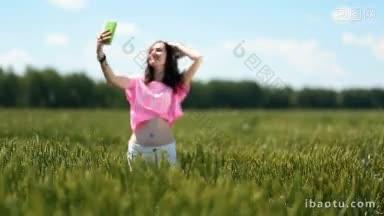 年轻漂亮的褐发女子穿着短裤正在农村的绿色麦田上用智能手机自拍，她正在纺纱